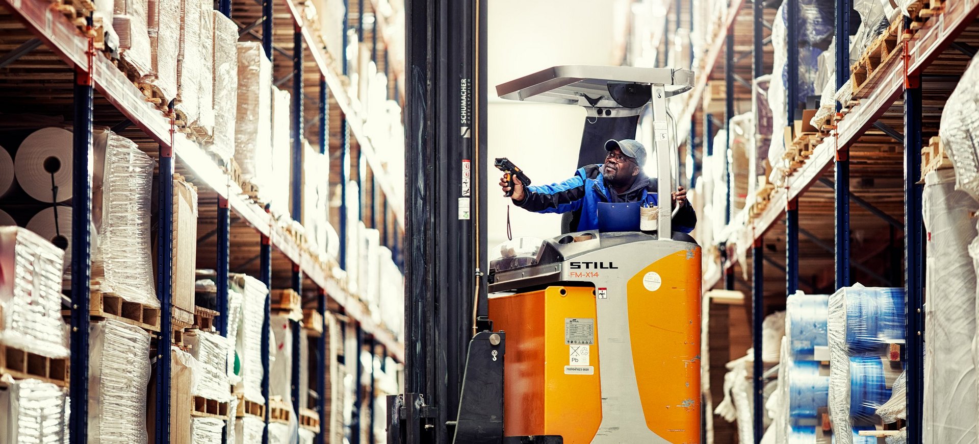 Logistikmitarbeiter mit Scanner auf Gabelstapler im Cella-Hochregallager bei der Kommissionierung