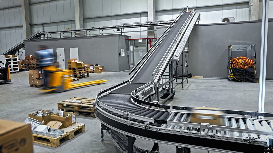 Fördertechnik im Logistikzentrum Cella Meppen mit Förderband und bewegtem Mitarbeitenden im Versandbereich