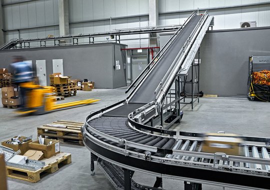 Fördertechnik im Logistikzentrum Cella Meppen mit Förderband und bewegtem Mitarbeitenden im Versandbereich